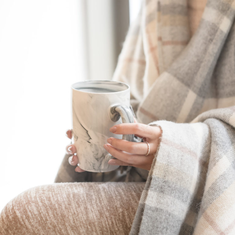 Women holding a mug, she is wearing a cozy blanket